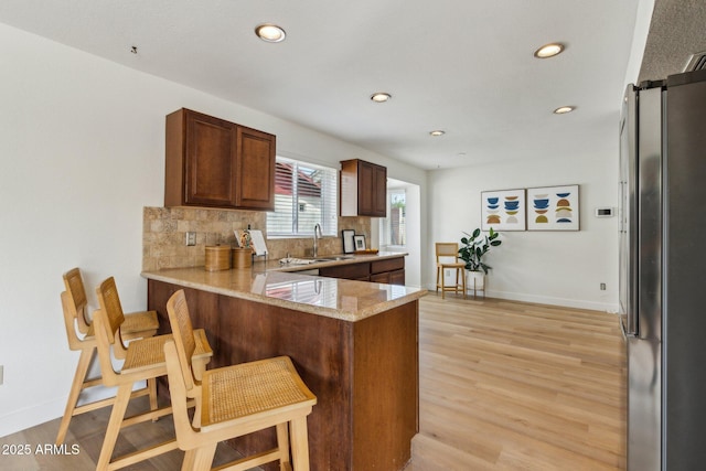 kitchen with a sink, freestanding refrigerator, a peninsula, a breakfast bar, and recessed lighting