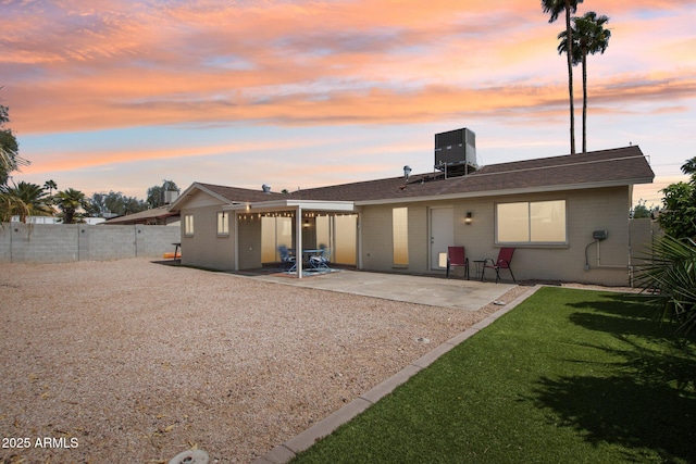 back of property at dusk with central AC, fence, a patio, brick siding, and a lawn