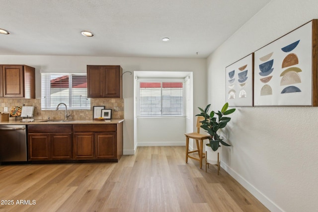 kitchen featuring stainless steel dishwasher, light wood-style floors, baseboards, tasteful backsplash, and a sink