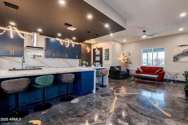 kitchen with wall chimney range hood, blue cabinets, backsplash, a sink, and a breakfast bar