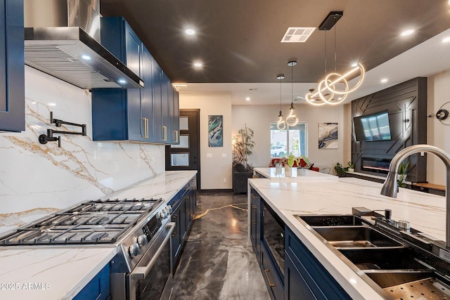kitchen with blue cabinetry, stainless steel range with gas cooktop, a sink, wall chimney exhaust hood, and tasteful backsplash