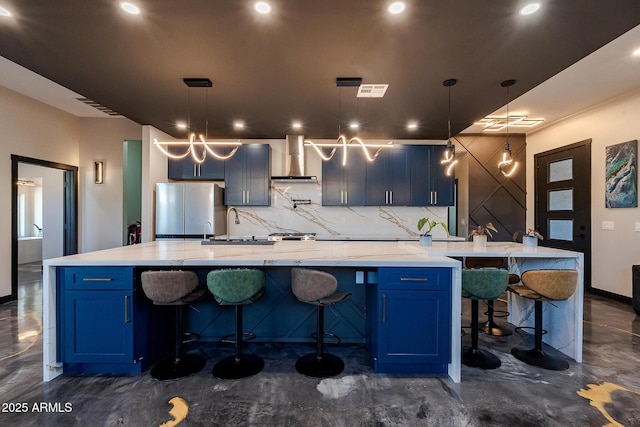 kitchen with freestanding refrigerator, wall chimney exhaust hood, tasteful backsplash, blue cabinets, and recessed lighting