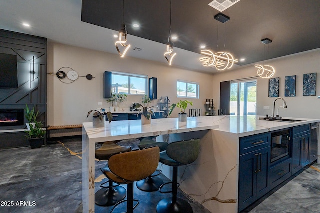 kitchen featuring a sink, blue cabinets, a large island, black microwave, and light stone countertops
