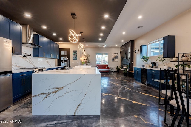 kitchen with a sink, wall chimney range hood, blue cabinetry, tasteful backsplash, and freestanding refrigerator