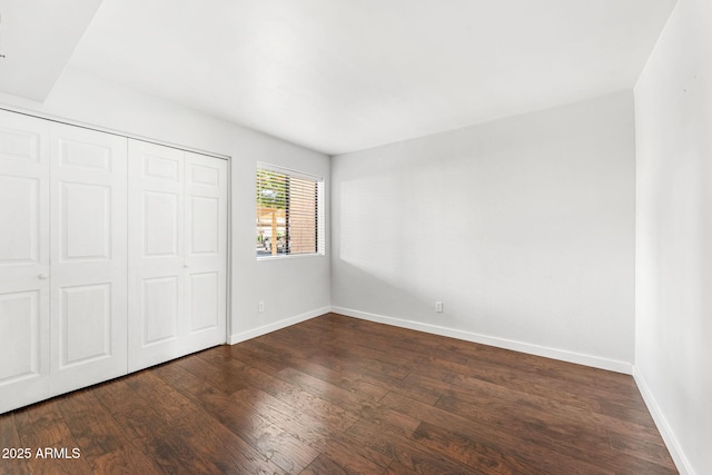 unfurnished bedroom with dark wood finished floors, baseboards, and a closet