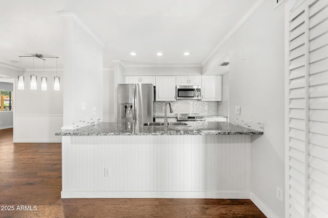 kitchen featuring a sink, dark wood-style floors, stainless steel appliances, dark stone counters, and a peninsula