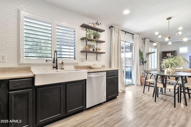 kitchen featuring dark cabinets, light wood-style flooring, a sink, stainless steel dishwasher, and tasteful backsplash