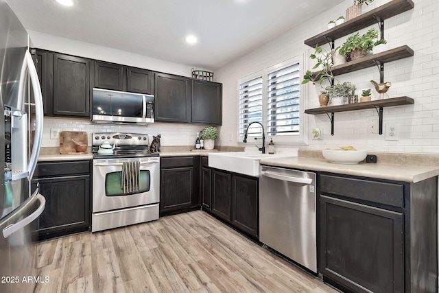 kitchen featuring a sink, open shelves, light wood-style floors, appliances with stainless steel finishes, and light countertops