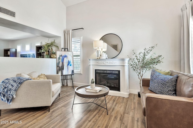 living area with visible vents, baseboards, a glass covered fireplace, and wood finished floors