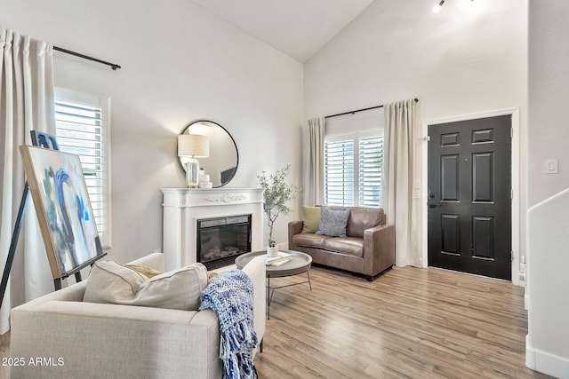 living room featuring a glass covered fireplace, high vaulted ceiling, and wood finished floors