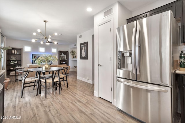 interior space featuring visible vents, baseboards, stainless steel fridge with ice dispenser, light wood-type flooring, and a notable chandelier