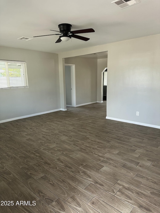 empty room with baseboards, visible vents, dark wood-style flooring, and arched walkways