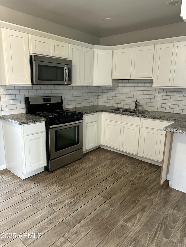 kitchen with a sink, appliances with stainless steel finishes, dark wood finished floors, and white cabinets