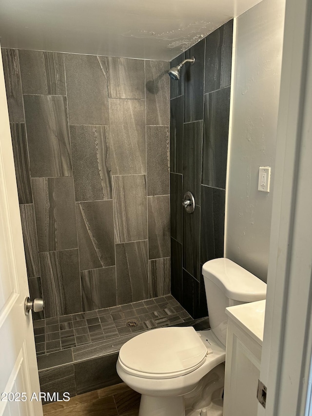 full bath featuring tiled shower, toilet, wood finished floors, and vanity