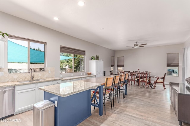557 S Lemon Ct, Gilbert, AZ 85296 - kitchen with stainless steel dishwasher, white cabinetry, a ceiling fan, backsplash, and a kitchen bar