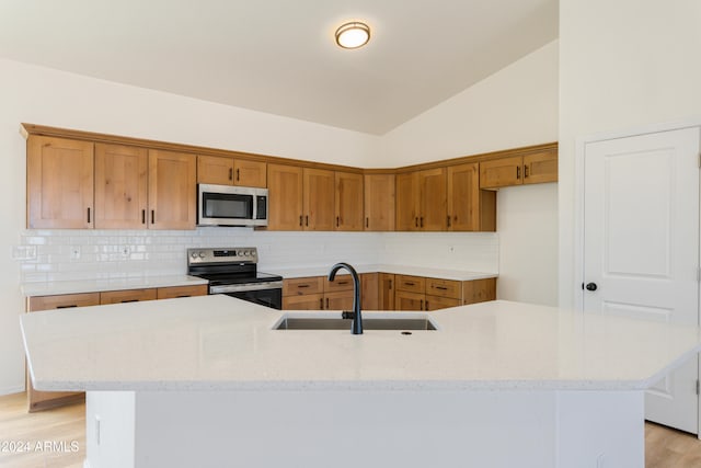 kitchen featuring sink, an island with sink, light hardwood / wood-style floors, vaulted ceiling, and appliances with stainless steel finishes