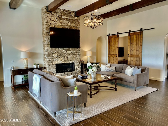 living room featuring a chandelier, beamed ceiling, a stone fireplace, and a barn door