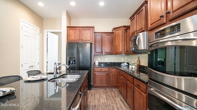 kitchen with dark stone countertops, hardwood / wood-style floors, sink, and black appliances