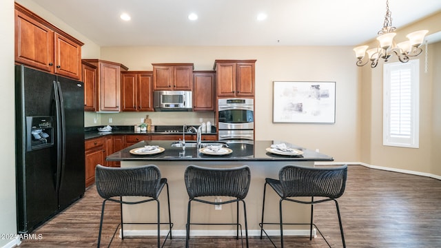 kitchen with a notable chandelier, stainless steel appliances, a center island with sink, and dark hardwood / wood-style floors