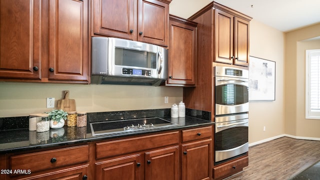 kitchen with appliances with stainless steel finishes, wood-type flooring, and dark stone countertops