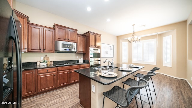 kitchen with black appliances, light hardwood / wood-style flooring, a center island with sink, sink, and a notable chandelier