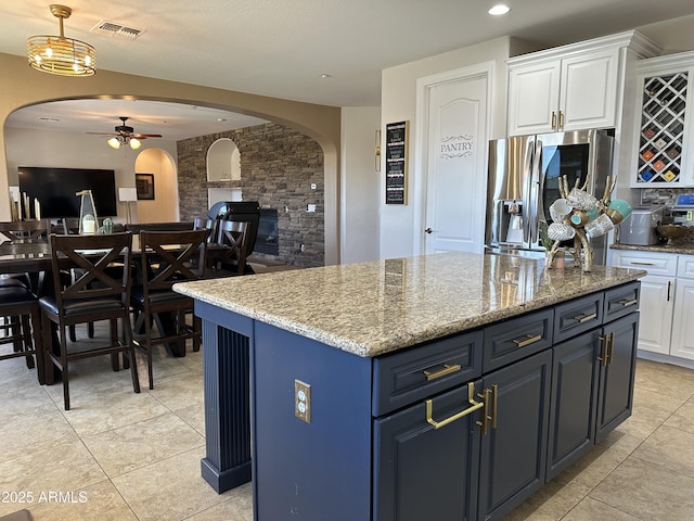 kitchen featuring visible vents, a ceiling fan, stainless steel refrigerator with ice dispenser, arched walkways, and white cabinets