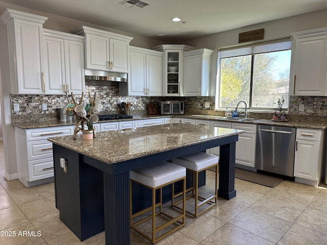 kitchen featuring visible vents, under cabinet range hood, stainless steel dishwasher, white cabinetry, and decorative backsplash