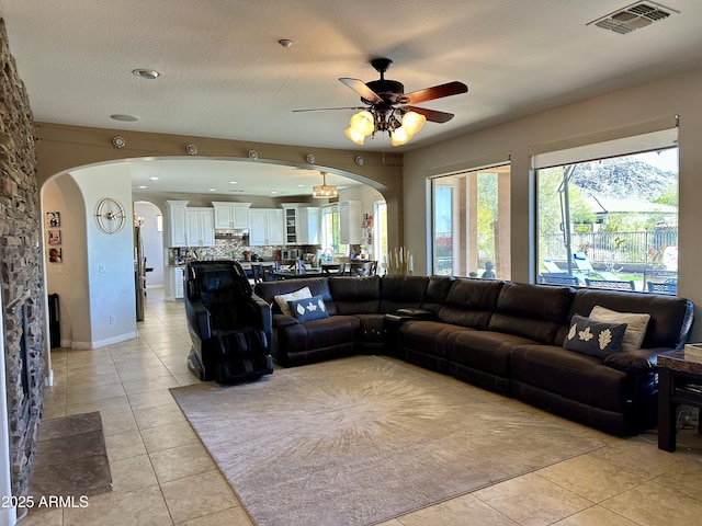 living area featuring a ceiling fan, light tile patterned floors, arched walkways, and visible vents