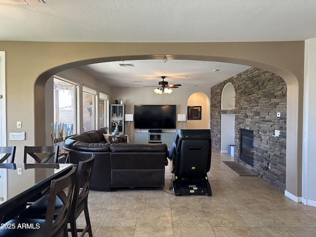 living area with baseboards, visible vents, ceiling fan, a stone fireplace, and a textured ceiling