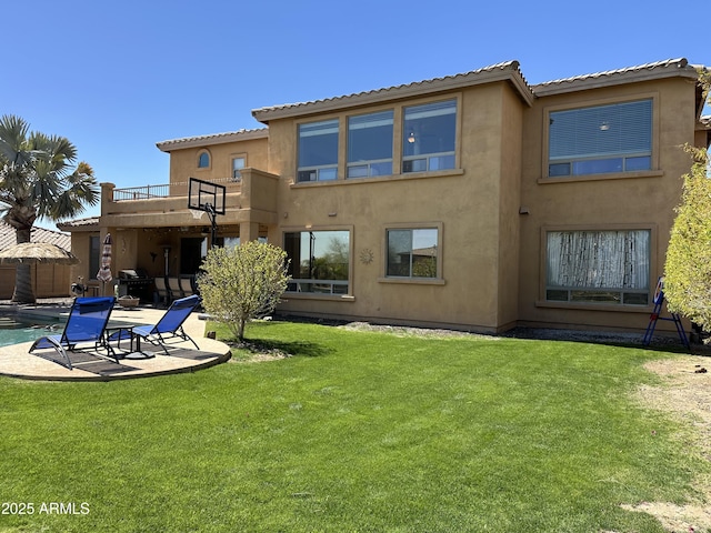 rear view of house with stucco siding, a lawn, an outdoor pool, a balcony, and a patio area