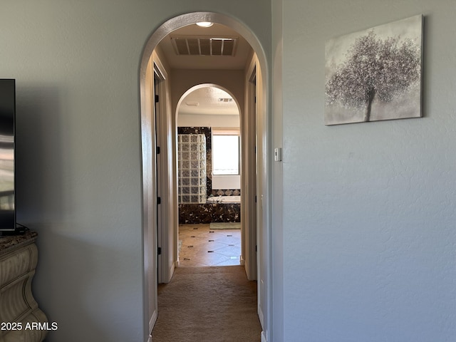 hallway featuring visible vents, arched walkways, and carpet floors