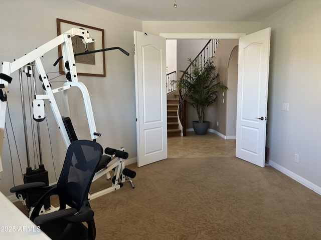 exercise area featuring arched walkways, carpet flooring, and baseboards