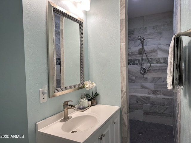 full bath featuring vanity, a textured wall, and tiled shower