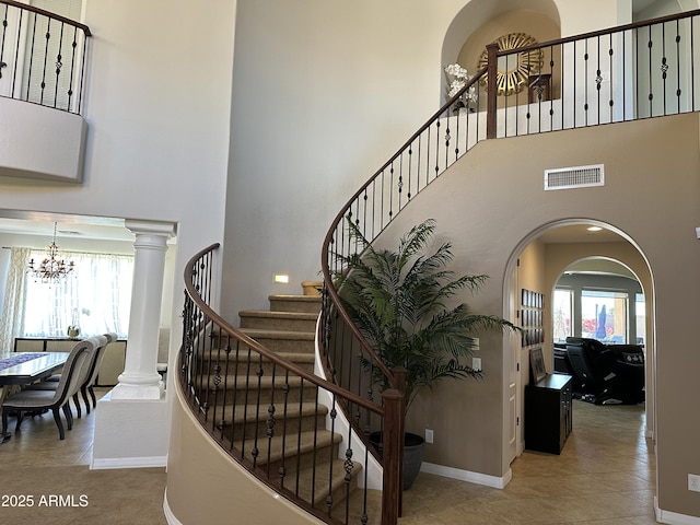staircase with visible vents, a notable chandelier, a healthy amount of sunlight, and a towering ceiling