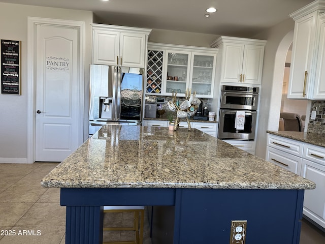 kitchen with stone counters, a kitchen island, arched walkways, appliances with stainless steel finishes, and white cabinetry