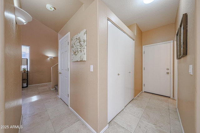 hallway featuring light tile patterned floors, baseboards, and vaulted ceiling