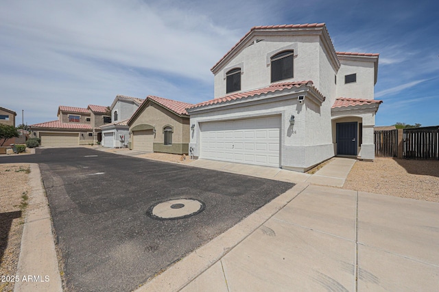 mediterranean / spanish-style house featuring a tile roof, fence, aphalt driveway, an attached garage, and stucco siding