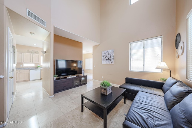 living area with visible vents, baseboards, light tile patterned floors, and a high ceiling