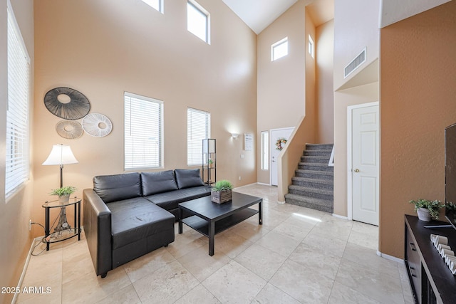 living area featuring a high ceiling, visible vents, baseboards, and stairway