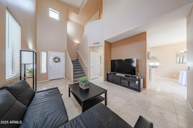 living room with visible vents, a towering ceiling, light tile patterned flooring, baseboards, and stairway