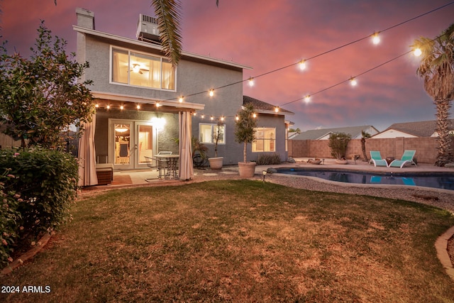 back house at dusk featuring a patio, a fenced in pool, a yard, and french doors