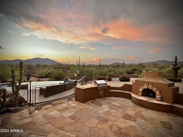 patio terrace at dusk featuring exterior kitchen, a mountain view, and area for grilling