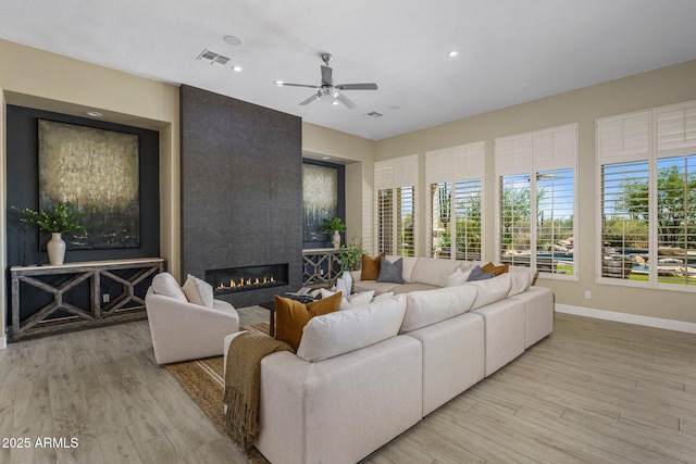 living area with a ceiling fan, light wood-type flooring, baseboards, a fireplace, and recessed lighting