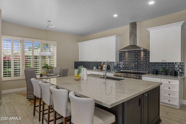 kitchen with wall chimney exhaust hood, a sink, tasteful backsplash, white cabinetry, and recessed lighting