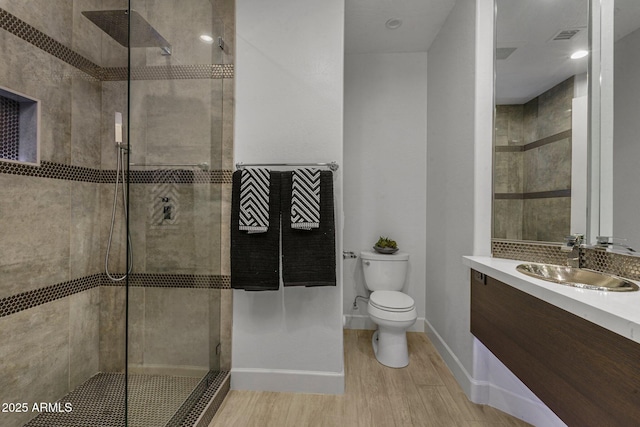 full bath with tiled shower, wood finished floors, toilet, and vanity