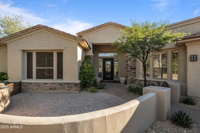 view of exterior entry featuring stone siding and stucco siding