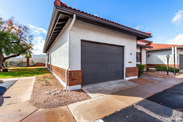 view of home's exterior featuring concrete driveway, a tiled roof, an attached garage, and stucco siding