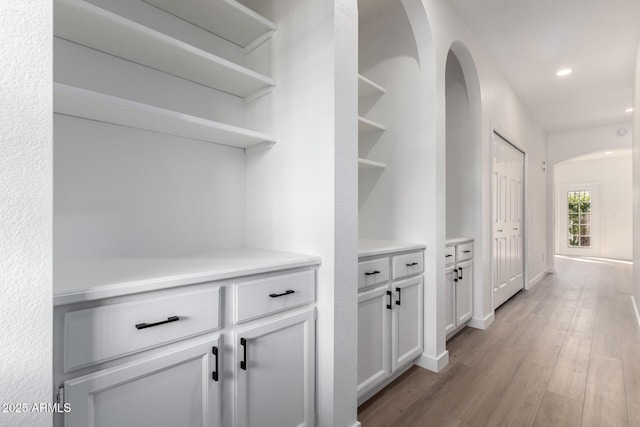 hall with arched walkways, recessed lighting, light wood-type flooring, and baseboards