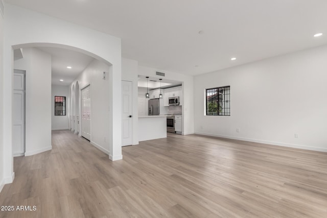 unfurnished living room featuring light wood-style flooring, recessed lighting, arched walkways, and visible vents