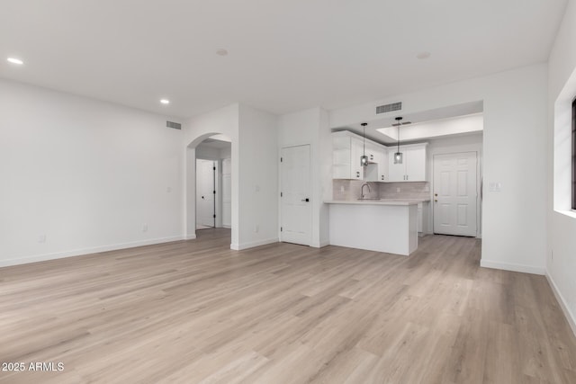 unfurnished living room with arched walkways, visible vents, baseboards, and light wood-style floors